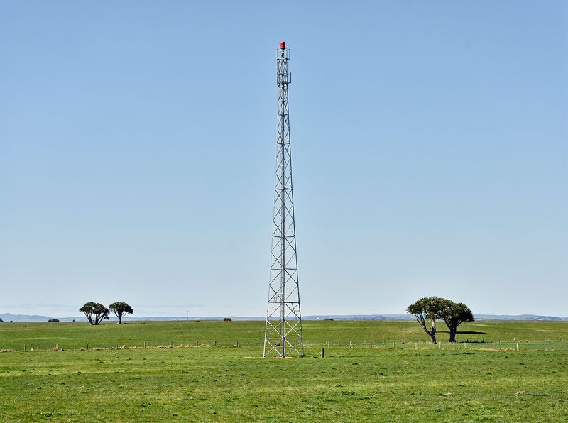 A steel lattice radio mast with a red beacon, standing on flat farmland